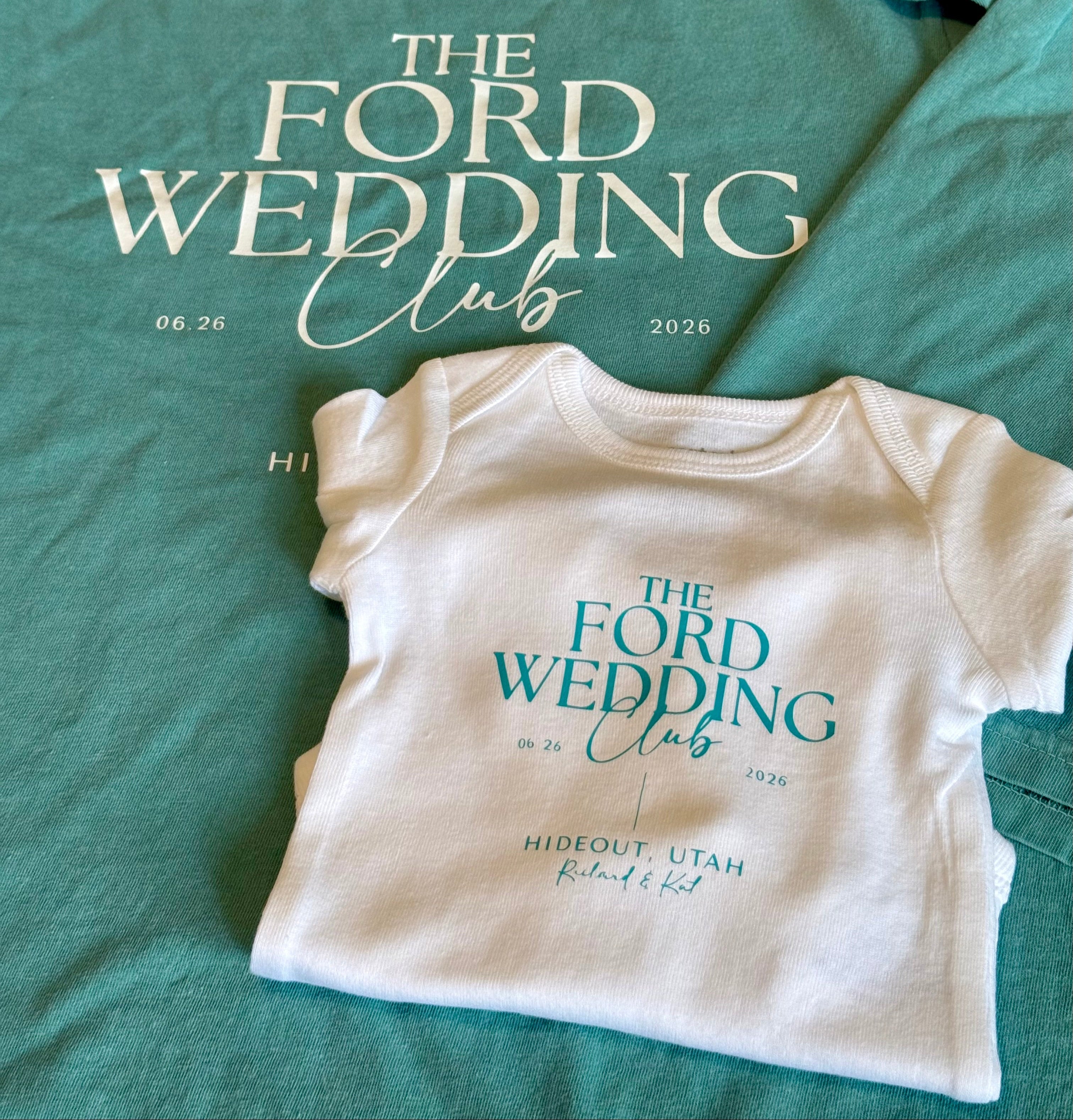 A matching mother-and-child t-shirt and bodysuit set laid flat. The larger adult-sized shirt is teal with white text reading 'THE FORD WEDDING Club' and small dates, while the smaller child-sized bodysuit is white with teal text reading 'THE FORD WEDDING Club' and 'HIDEOUT, UTAH' with a heart outline.