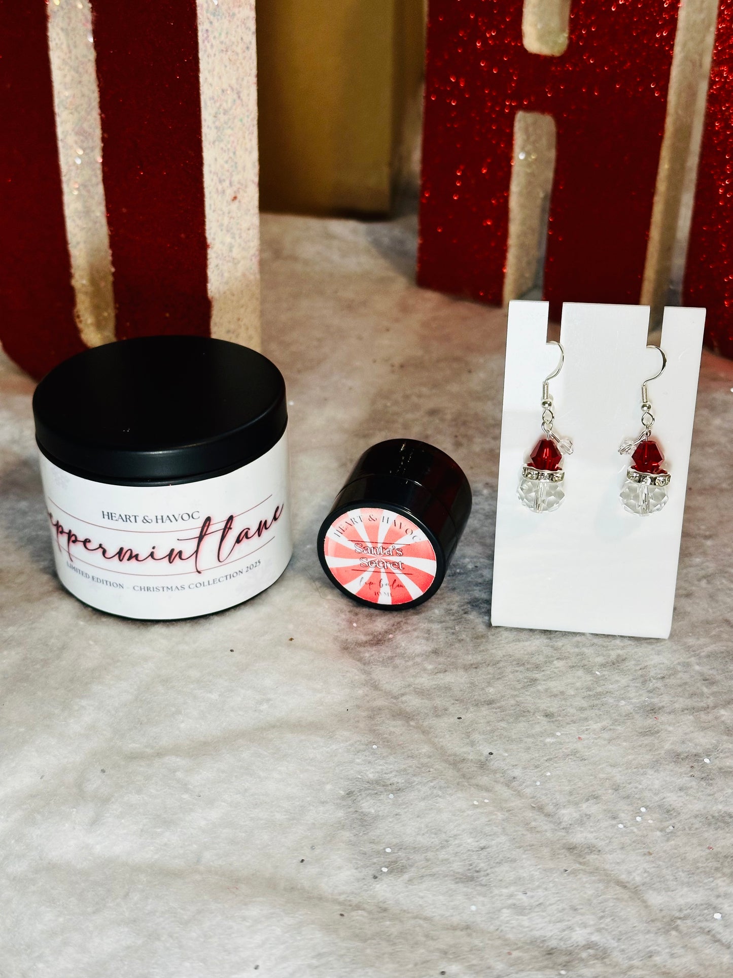 peppermint candle, lip balm and santa earrings on a textured surface with Christmas background.